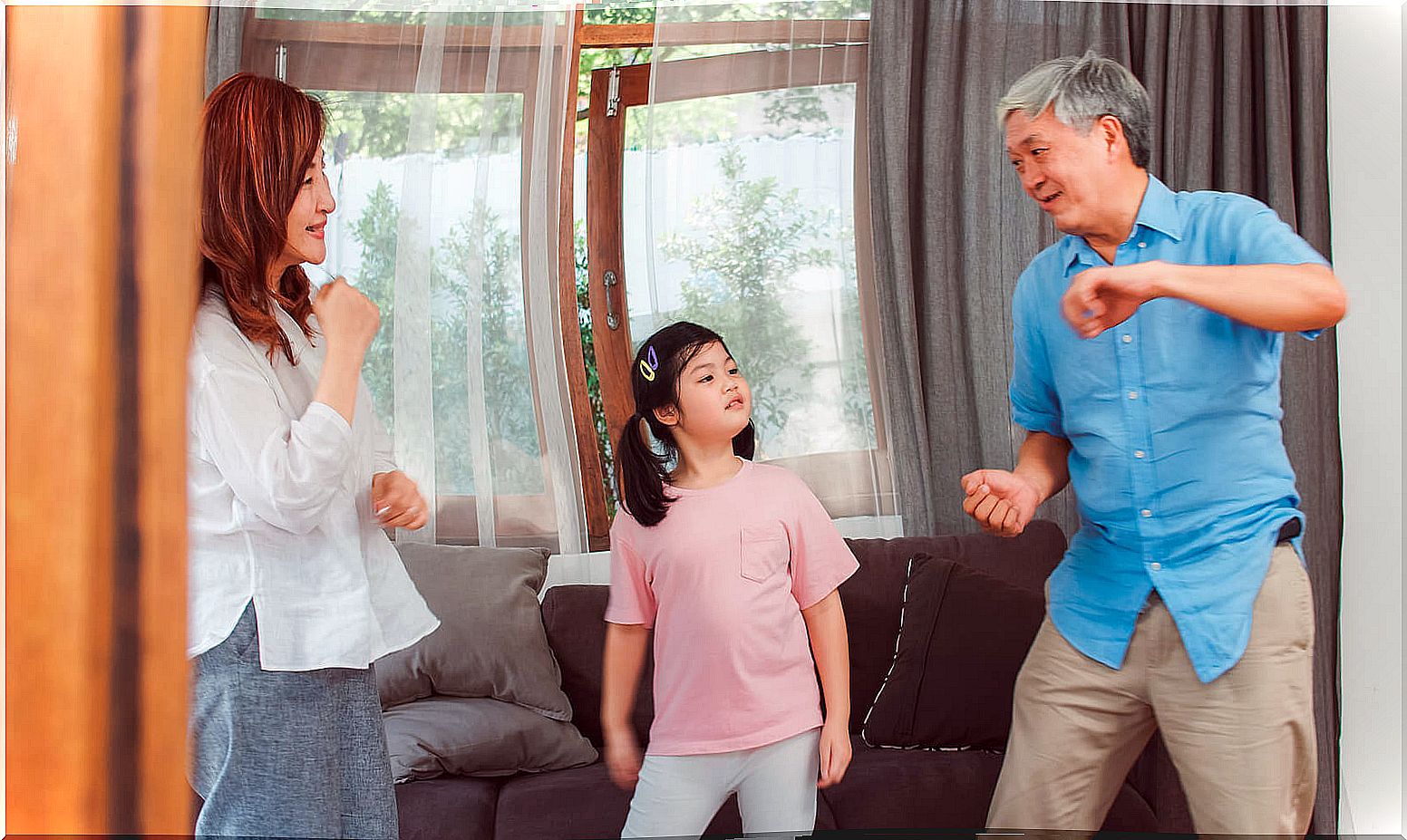 Parents dancing with their daughter in the living room practicing some music games.