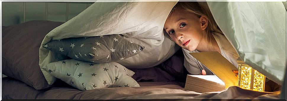 Girl reading one of the books in the Enigmas collection under the covers.