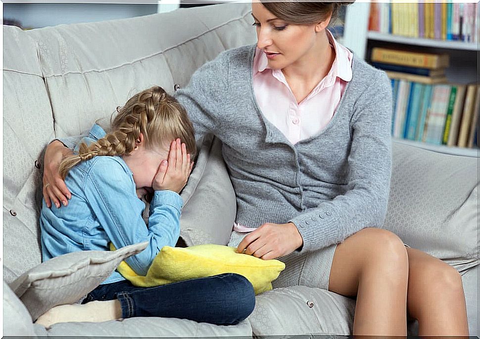 Little girl crying on the sofa with her mother comforting her.