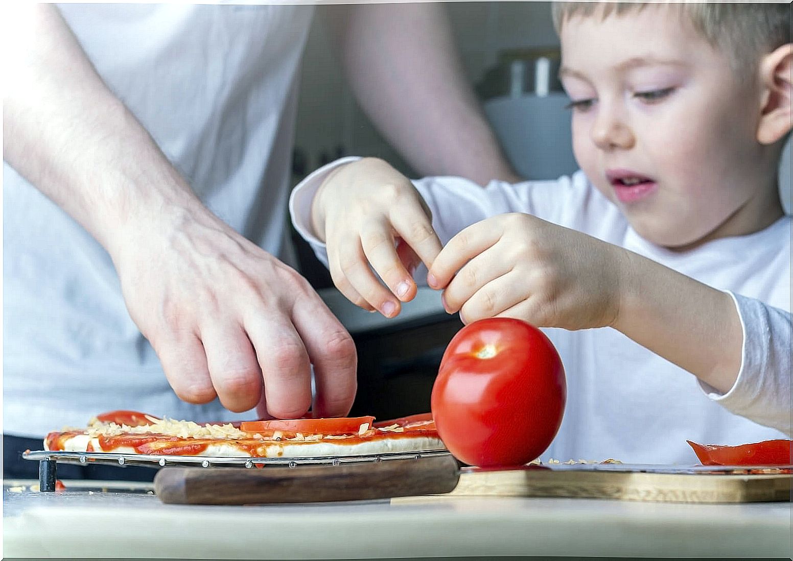 Boy helping his father cook a pizza.