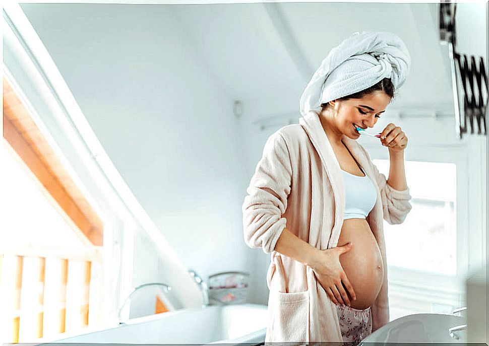 Pregnant woman after getting out of the shower brushing her teeth for good oral health during pregnancy.