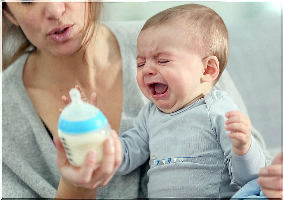 Mother trying to bottle her baby who cries from the ambivalent attachment he receives.