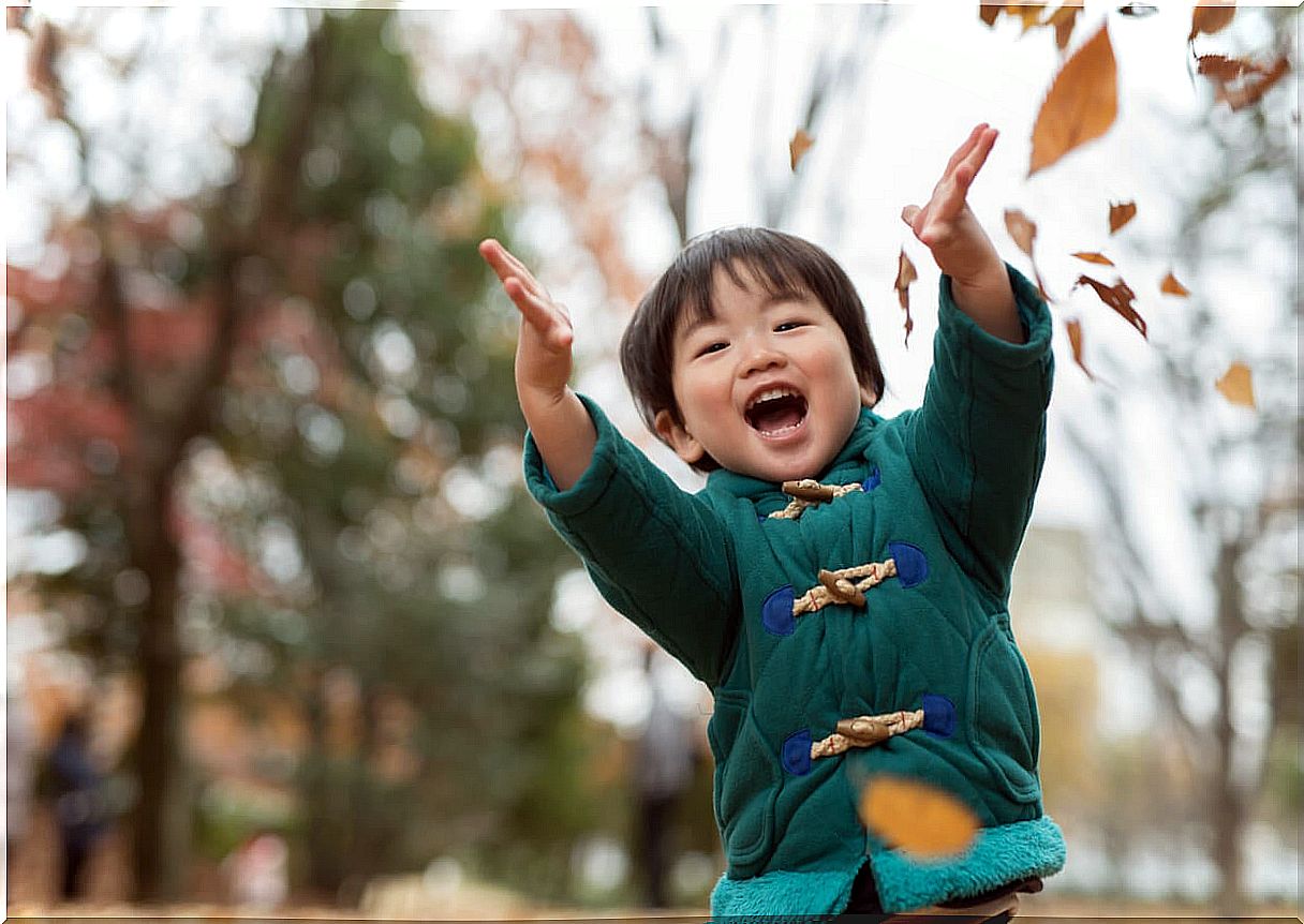 3 year old boy playing with leaves in the park.