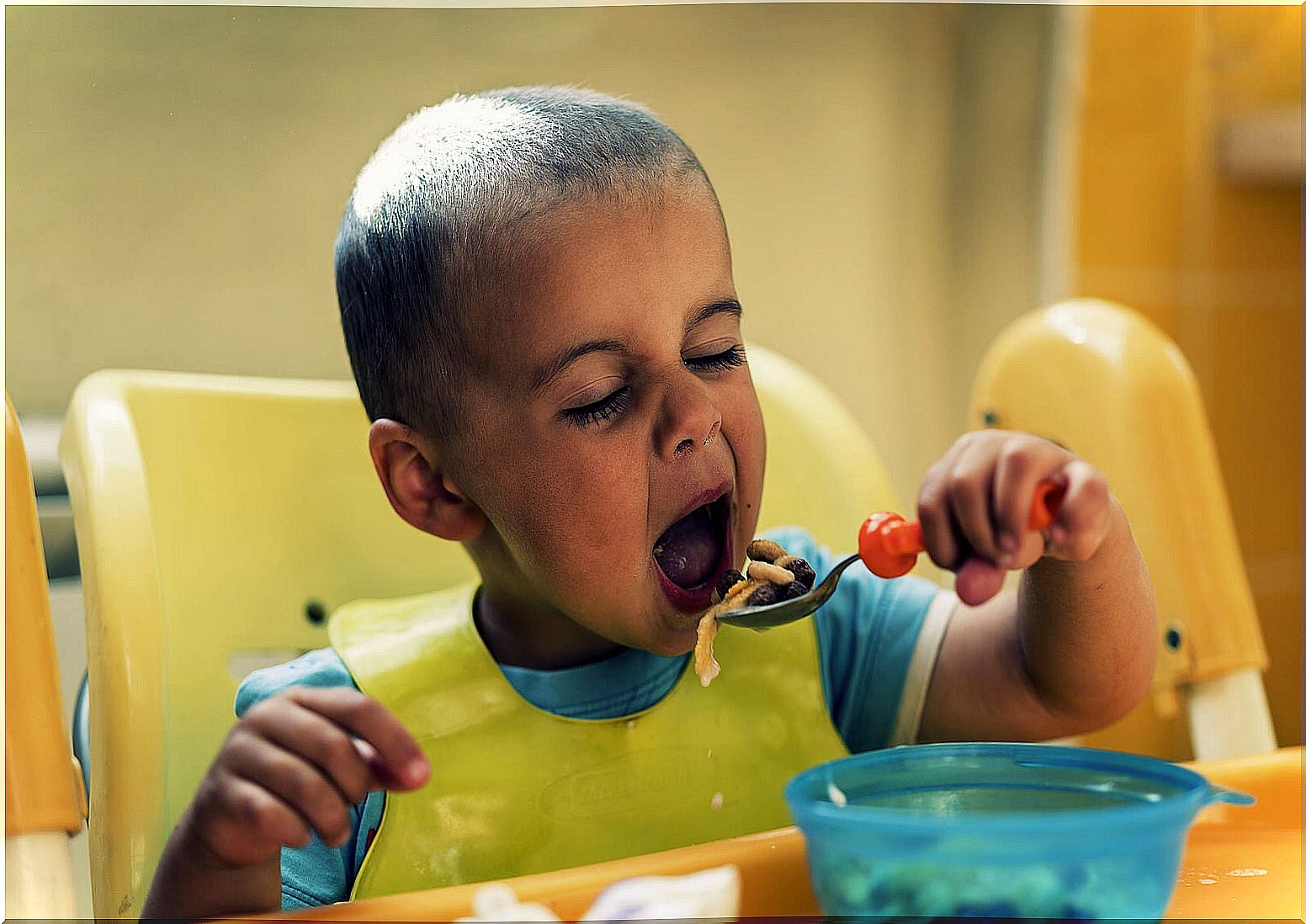 2 year old boy eating with a spoon by himself.