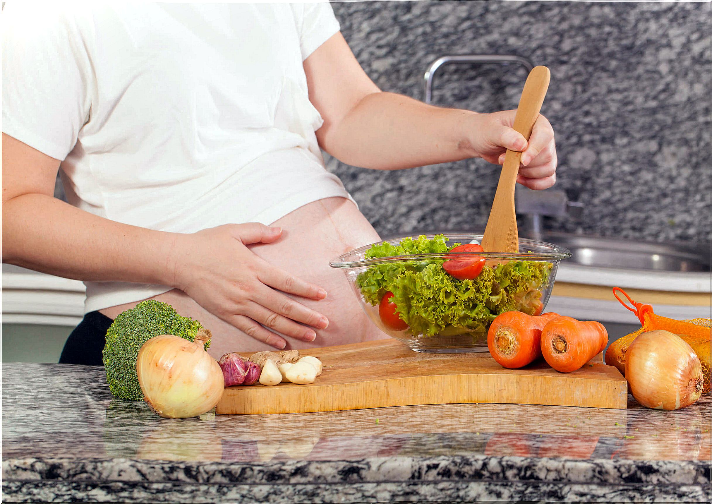 Pregnant woman making herself a salad with green leafy vegetables.